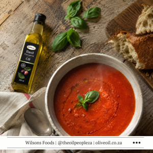 Roasted tomato soup with a swirl of Wilson's Foods Basil Oil in a white bowl with crusty bread alongside